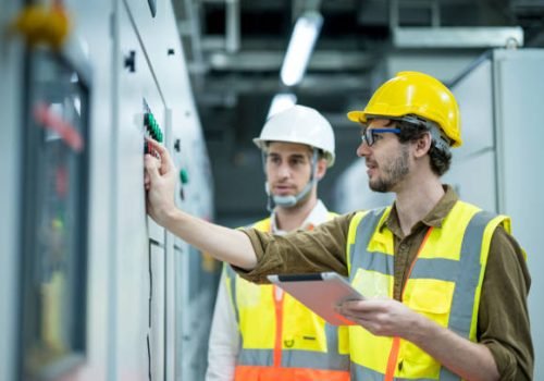Industrial service electrician engineers standing side by side having exchange idea in front of electricity control board. Energy management system (EMS) concept.