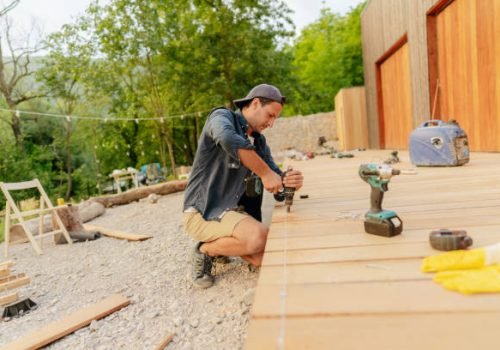 Photo of a carpenter installing wooden decking in front of a cabin house