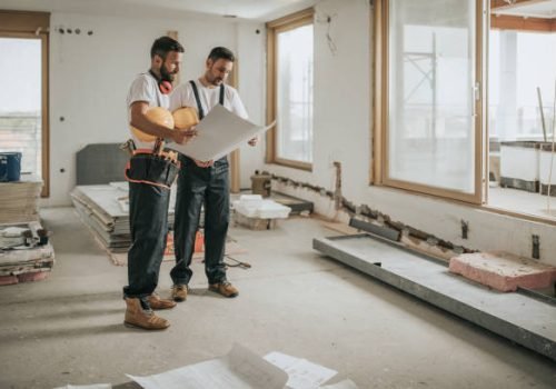 Young manual workers standing at construction site and examining blueprints.